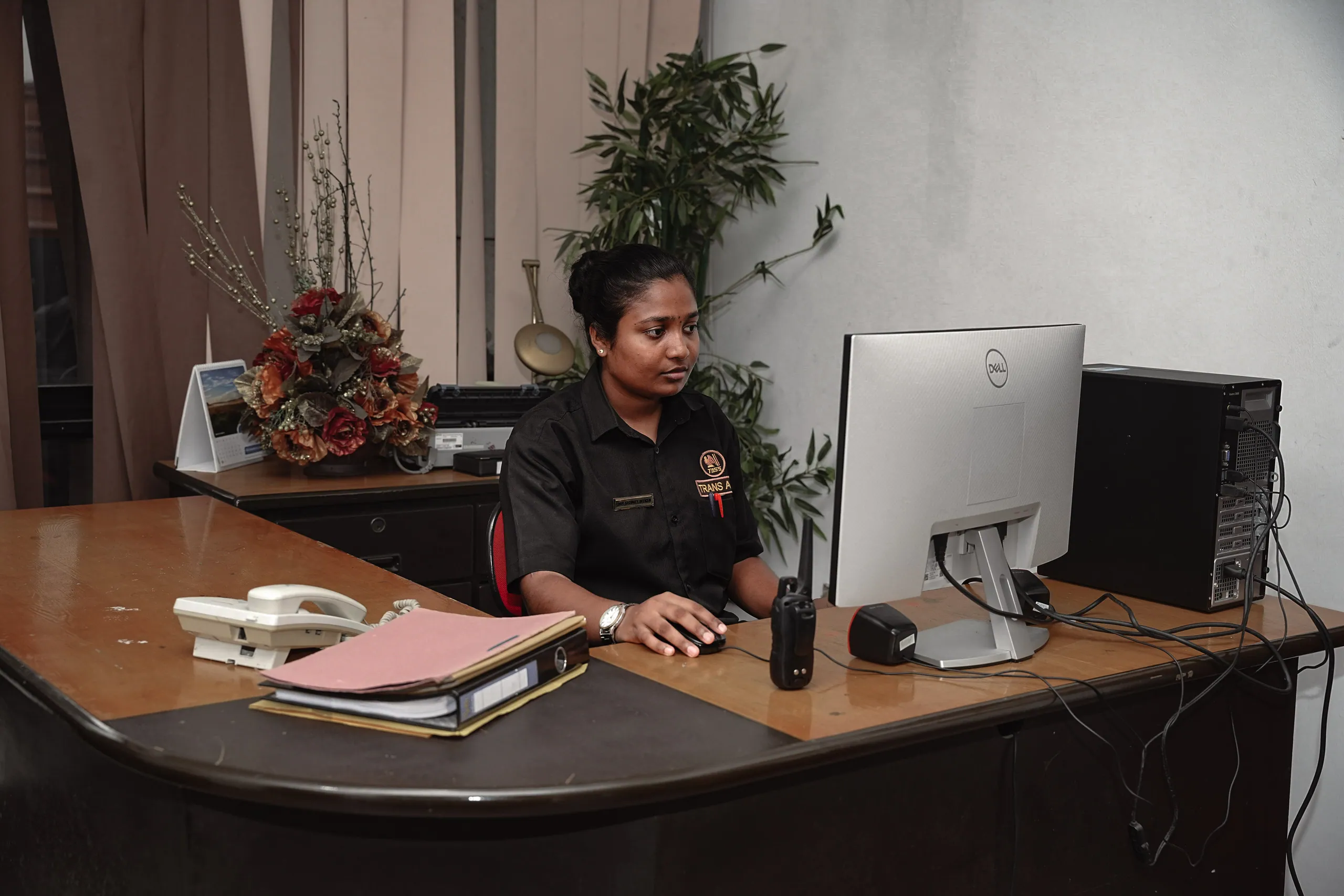 Trans Asia officer at a client reception desk, working at a computer beside a visitor log, telephone and radio