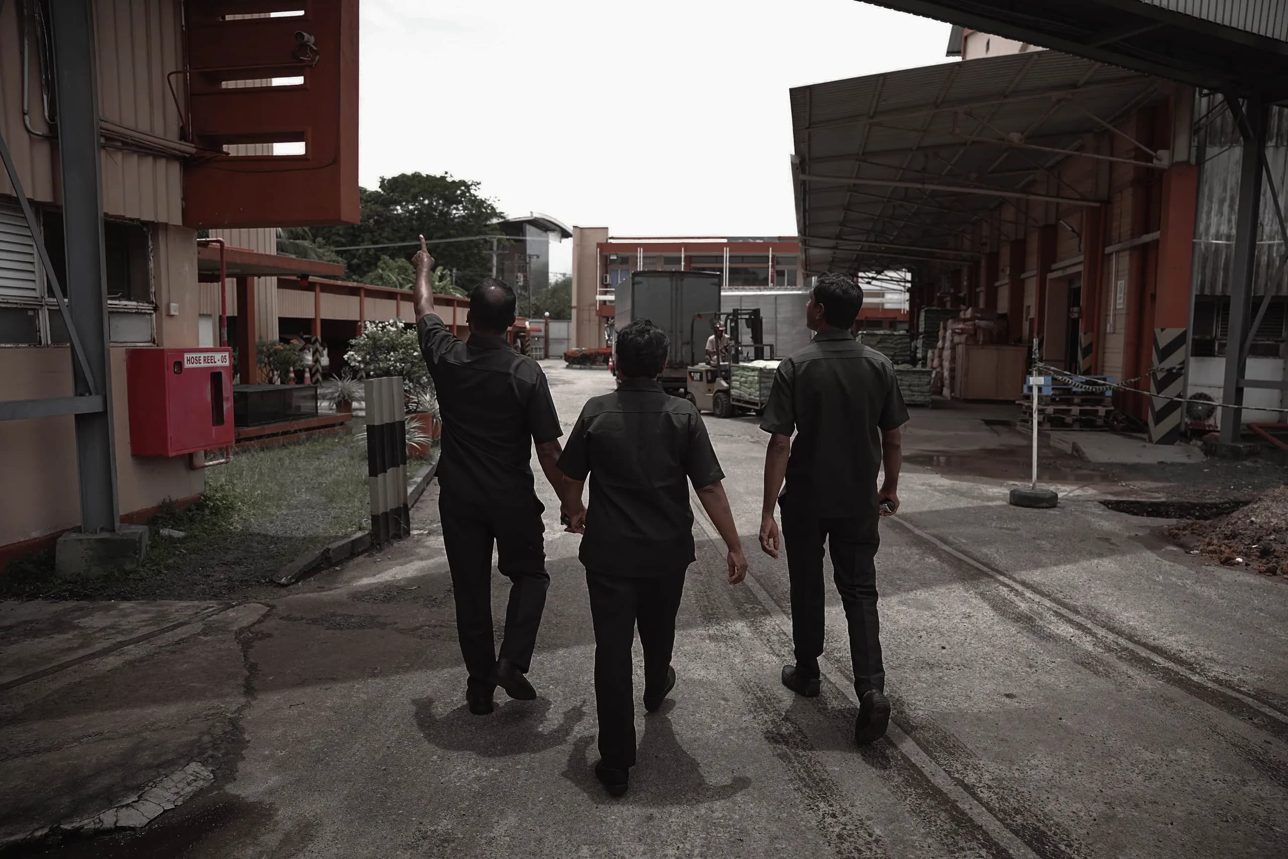 A supervisor walking through a factory yard with two officers, pointing out a detail of the site